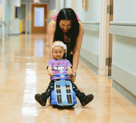 Young cancer patient on a riding toy in the hospital hallway